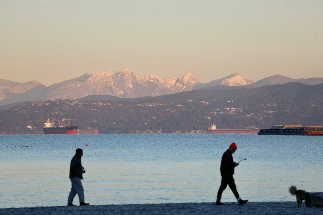 Pedestrians walking near the seawall with Vancouver's glass skyline and mountains behind