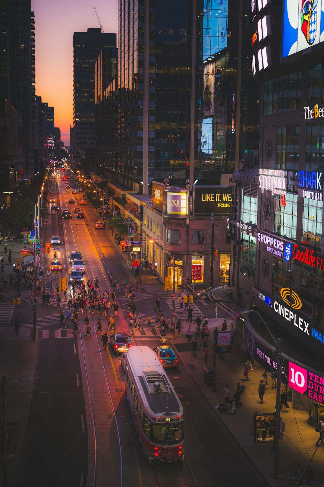Crowd of pedestrians crossing a busy downtown Toronto street at dusk
