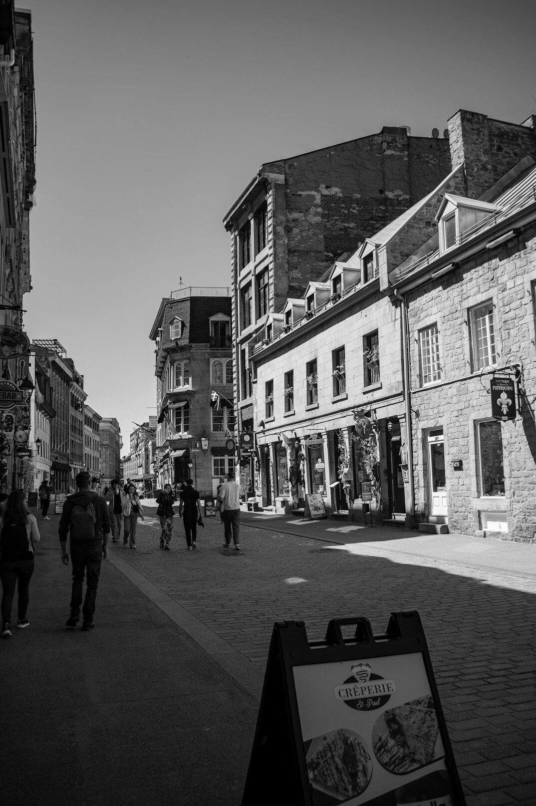 People walking through a cobblestone lane in Old Montreal lined with cafes