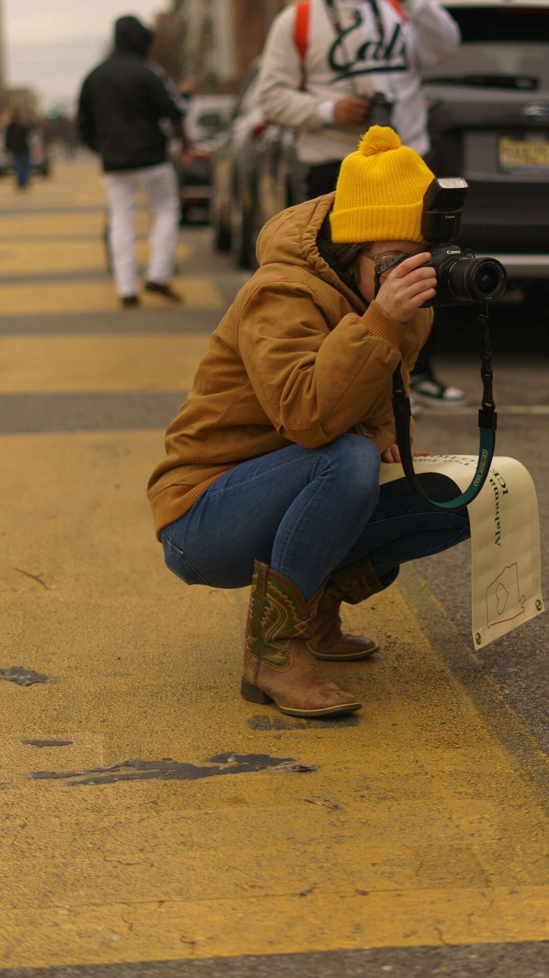 Black Canadian street photographer crouched down taking a photo with a film camera
